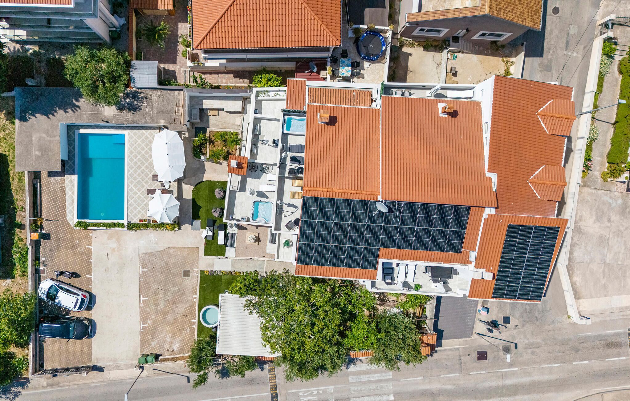 Ovenudblik over en bolig med swimmingpool, solpaneler og en overdækket terrasse.