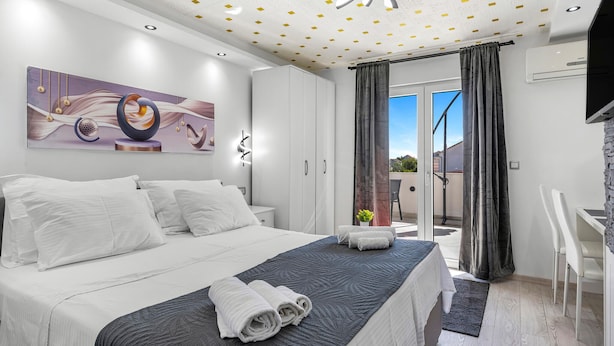A modern bedroom with a large bed, a ceiling with a geometric pattern, a painting on the wall, and a view through the glass door.