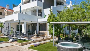 A modern two-story house with a patio area, outdoor seating, and a hot tub.