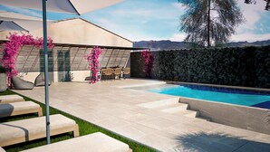 Un área de piscina moderna al aire libre con un patio de piedra, sillas de descanso y un comedor.