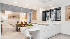 Una cocina moderna con una isla central, armarios blancos y un comedor con mesa y sillas de madera.