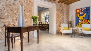 Una habitación con paredes de piedra, una mesa de comedor de madera con sillas, un sofá blanco y un cuadro colorido.