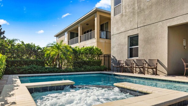 Ein Swimmingpool mit Whirlpool, umgeben von einer Terrasse mit Stühlen und einem Gebäude mit Balkonen.