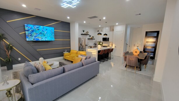 A modern living room with a grey sofa, yellow chairs, and a flat-screen TV on the wall. - Modern 3BR • 3.5 Bath • Near Downtown • Sleeps 10 (Houston)