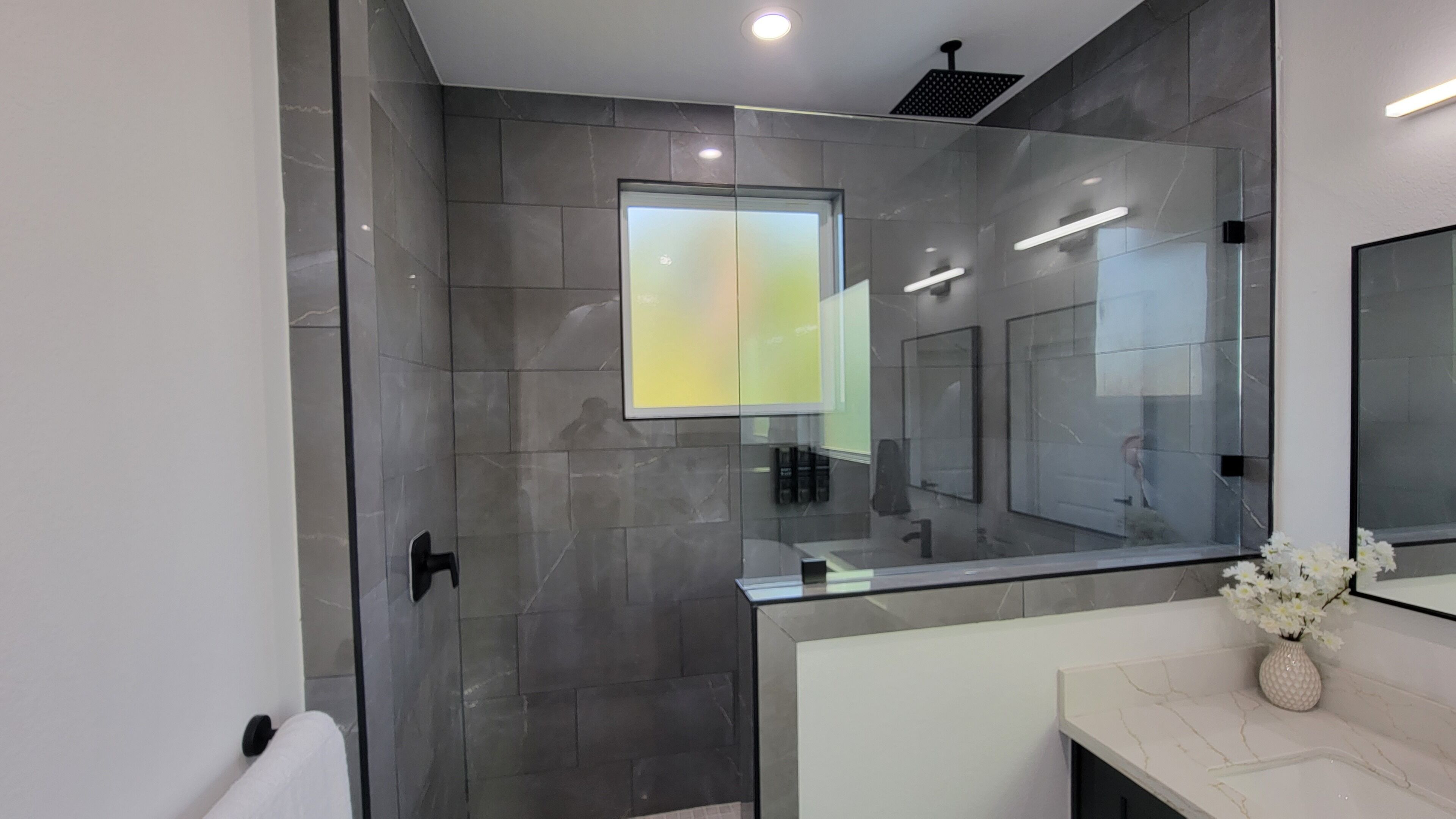 Een moderne badkamer met een douchecabine van glas, een grote spiegel en een marmeren aanrechtblad.