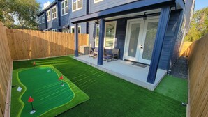 A backyard with artificial grass, a patio area with seating, and a wooden fence. - Modern 3BR • 3.5 Bath • Near Downtown • Sleeps 10 (Houston)