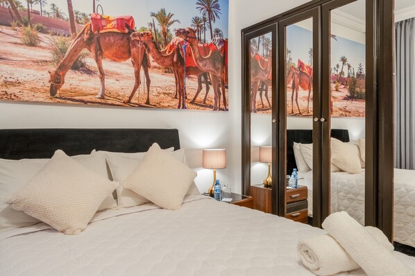 A hotel room with a large bed, pillows, a nightstand with a lamp, and a wall mural of camels. - Charming two-bedroom apartment in the centre of Marrakesh Gueliz (Marrakech)