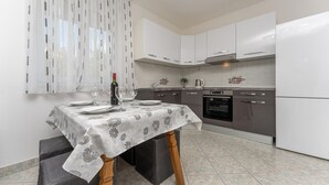 Una cocina moderna con armarios blancos, una mesa de comedor dispuesta con platos y copas de vino, y una botella de vino.