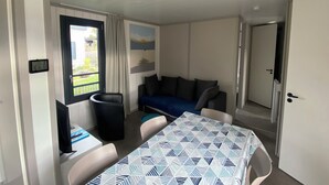 Une pièce comprenant une table, des chaises, un canapé, un téléviseur et une fenêtre avec des rideaux.