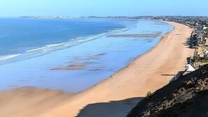 Une plage côtière avec un ciel dégagé, un rivage sablonneux et une vue lointaine sur la ville.