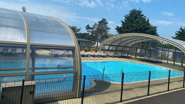 Une piscine couverte avec des chaises longues et une structure en verre.