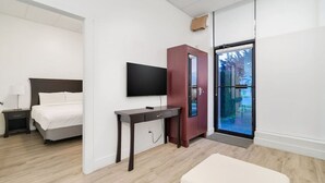 Een moderne hotelkamer met een bed, een bureau, een televisie, een kledingkast en een glazen schuifdeur naar een balkon.