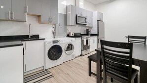 Een moderne keuken met grijze en witte kastjes, een ingebouwde magnetron, een wasmachine en een eethoek met een tafel en stoelen.
