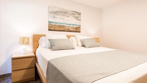 A neatly made bed with a grey blanket, two bedside lamps, and a painting of a beach scene on the wall. - Cozy apartment in Santa Margalida (Santa Margalida)