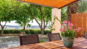 An outdoor patio with a wooden table and chairs, surrounded by lush greenery and a view of the landscape. - Cozy apartment in Santa Margalida (Santa Margalida)