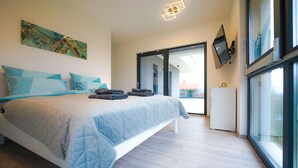 A modern bedroom with a large bed, a painting on the wall, a flat-screen TV, and a view through a glass door.
