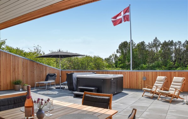 An outdoor patio with a wooden deck, a hot tub, lounge chairs, and a flag.