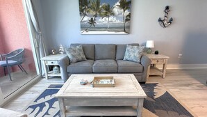 Een woonkamer met een grijze bank, twee bijzettafels, een salontafel en een strandafbeelding aan de muur.