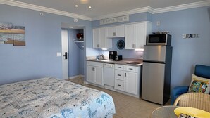 Un dormitorio compacto con cama, kitchenette con armarios blancos, refrigerador y microondas.