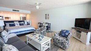 A modern living room with a bed, sofa, armchair, coffee table, dining table, chairs, and a TV. - Casa Playa #402 Beach Front - Turtle's Nest (Fort Myers Beach)