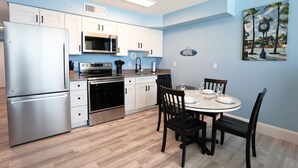 A modern kitchen with white cabinets, stainless steel appliances, and a dining area with a glass table and chairs. - Casa Playa #501 - One Bedroom Beach Front - Sand Dollar (Fort Myers Beach)