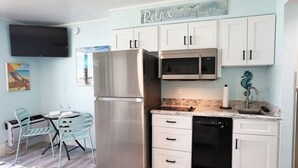 A modern kitchen with white cabinets, stainless steel appliances, and a dining area with a beach-themed painting. - Casa Playa #504 - Sea Horse (Fort Myers Beach)