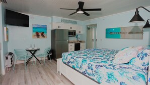 A compact hotel room with a bed, a desk with chairs, a kitchenette, and a ceiling fan. - Casa Playa #504 - Sea Horse (Fort Myers Beach)