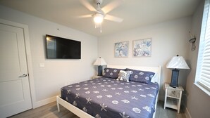Un dormitorio con cama, ventilador de techo, televisor montado en la pared, lámparas de noche y obras de arte.