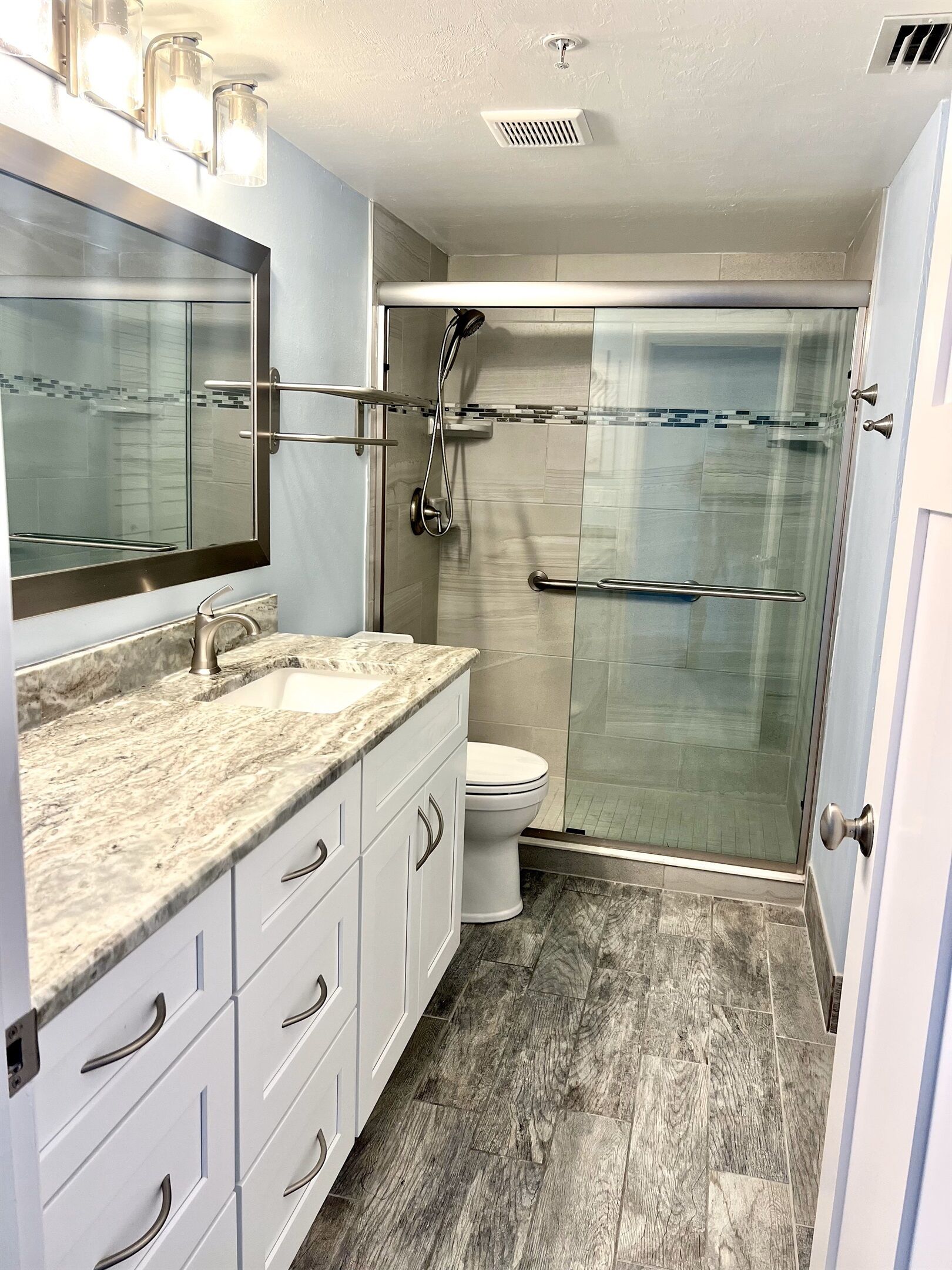 Une salle de bain moderne avec une douche à parois de verre, des toilettes blanches et un comptoir en marbre.