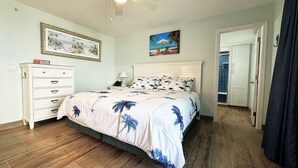 Ein Schlafzimmer mit Bett, Schminktisch, Nachttisch, einem gerahmten Bild und einer Tür zum Badezimmer.