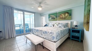 A bedroom with a bed, a bench, a nightstand, a ceiling fan, and a view of the outside.