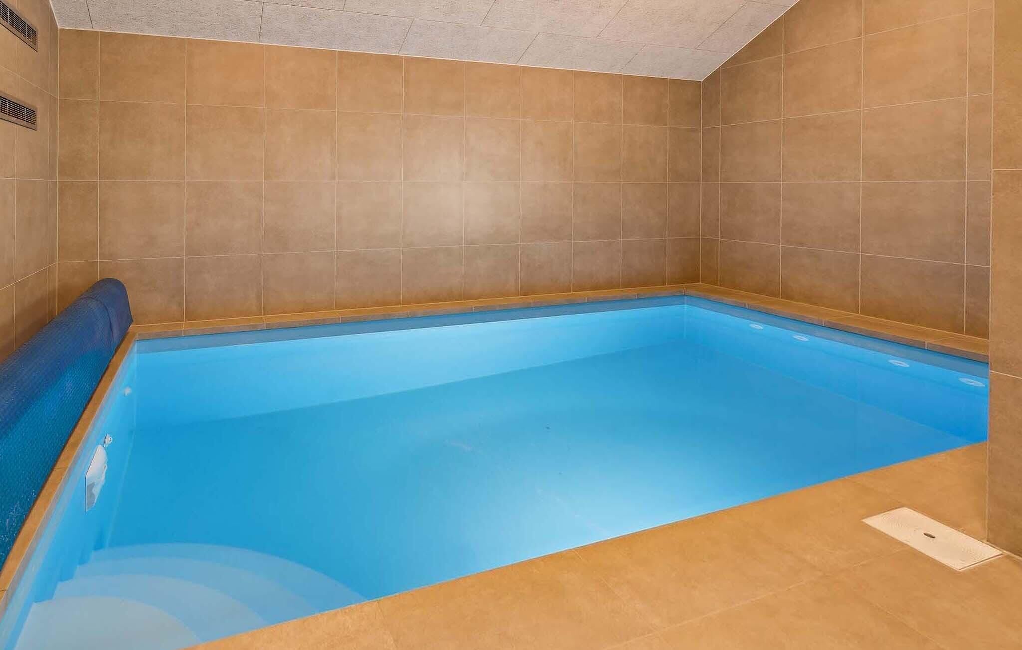 Une piscine intérieure rectangulaire, avec de l’eau bleue, entourée de murs recouverts de carreaux beiges.