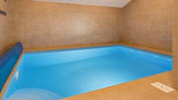 Une piscine intérieure rectangulaire, avec de l’eau bleue, entourée de murs recouverts de carreaux beiges.