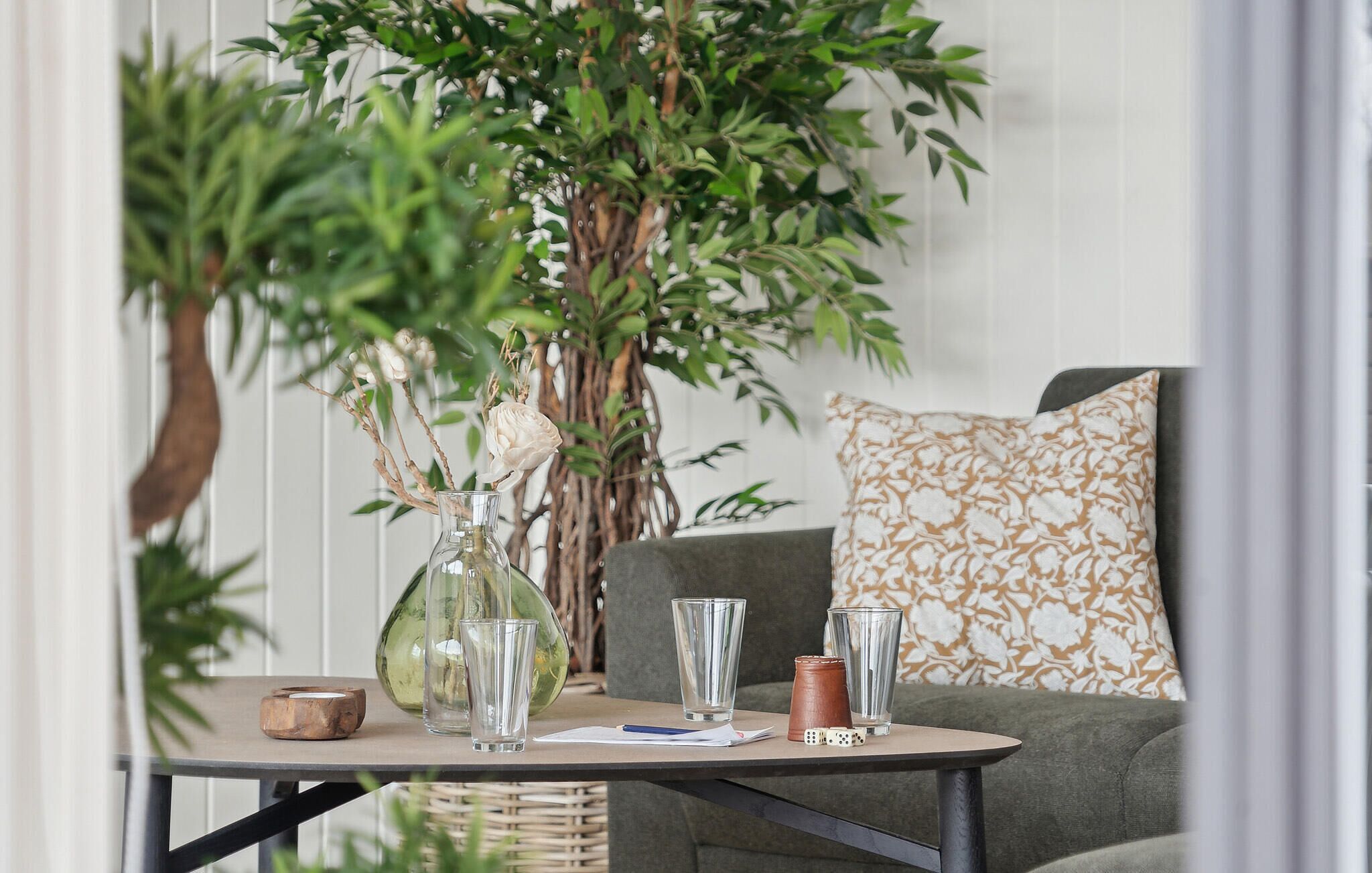Un coin salon confortable avec une table, un vase rempli de fleurs et une grande plante.