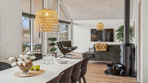 Ein modernes Wohnzimmer mit Essbereich, großen Fenstern, einem Flachbildfernseher und einem Kamin.