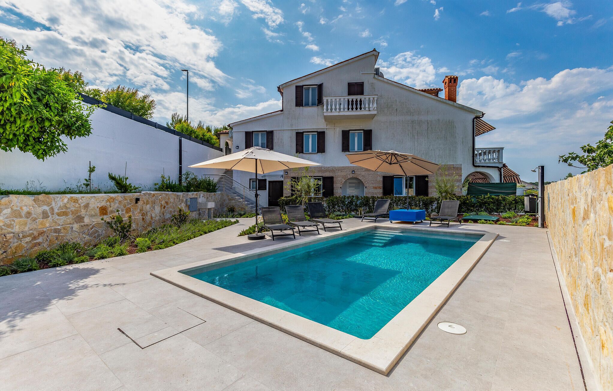 Uma casa de dois andares com piscina, área de estar externa e um muro de pedra.