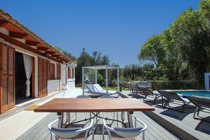 A wooden deck with a table and chairs, a pool, and a covered seating area with umbrellas.