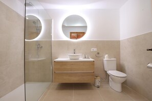 A modern bathroom with a glass-enclosed shower, a round mirror, a wooden vanity with a sink, and a toilet.