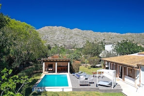 Ein Poolbereich mit Bergblick, eine überdachte Außenlounge und ein Gebäude mit einem Ziegeldach.