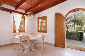 A dining area with a round table and four chairs, wooden beams on the ceiling, and a view of the outdoors through an arched doorway. - Villa Alegre (Pollensa / Pollença)