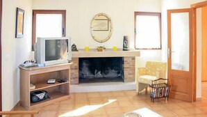 A living room with a fireplace, a television on a stand, a sofa, and a bookshelf.