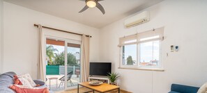 Uma sala de estar com televisão, sofá, mesa e varanda com vista.