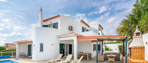 Uma vila branca com piscina, área de estar externa e um alpendre coberto.