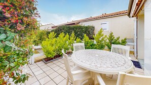 A patio with a round table and white chairs, surrounded by lush greenery and a white fence. - 1 bedroom awesome home in Vaux-sur-Mer (Vaux-sur-Mer)