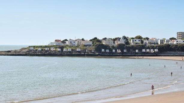 A coastal beach with a row of white houses, some with visible balconies, and a sandy beach area with people walking and swimming. - 1 bedroom awesome home in Vaux-sur-Mer (Vaux-sur-Mer)