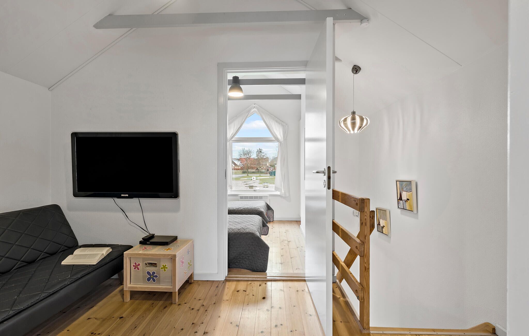 Een moderne kamer met een flatscreen televisie, een houten dressoir, een met kussens beklede bank en een houten trap naar een hoger niveau.