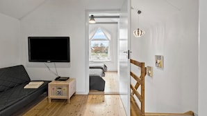 A modern room with a flat-screen TV, a wooden sideboard, a cushioned bench, and a wooden staircase leading to an upper level. - 3 bedroom gorgeous home in Hadsund (Hadsund)