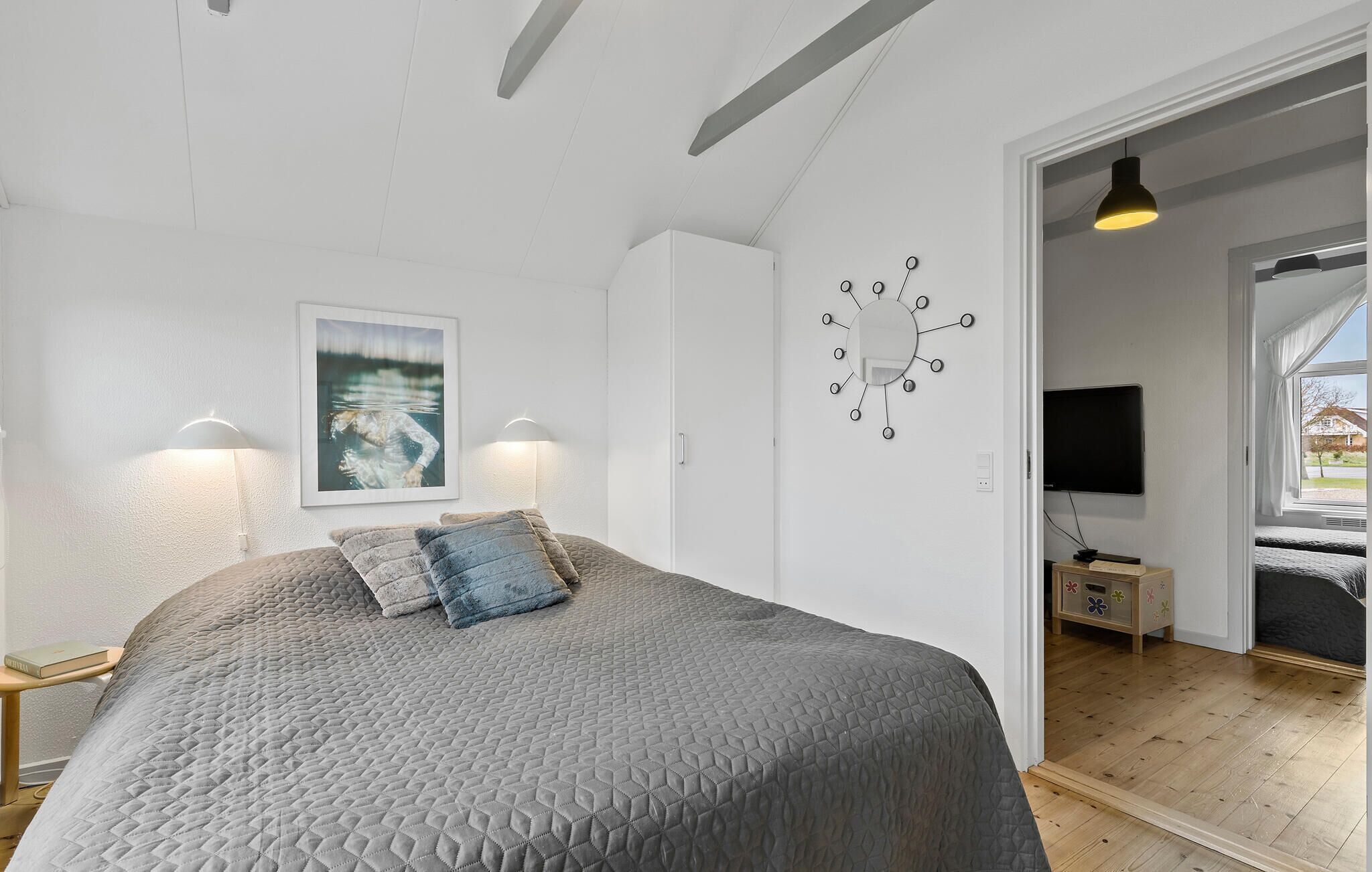 Een slaapkamer met een groot bed, een wandklok, een televisie en een raam met gordijnen.