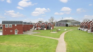 A row of red-roofed cottages with a central glass building, surrounded by a grassy area with a path. - 3 bedroom gorgeous home in Hadsund (Hadsund)