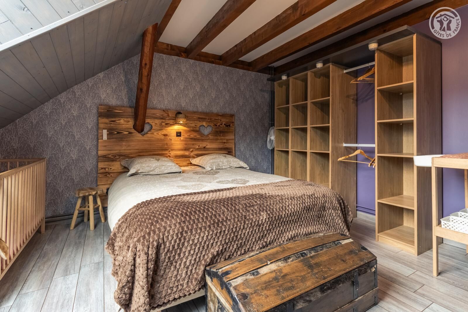 A cozy bedroom with a wooden headboard, a large bed, a wooden chest, and built-in wooden shelving.